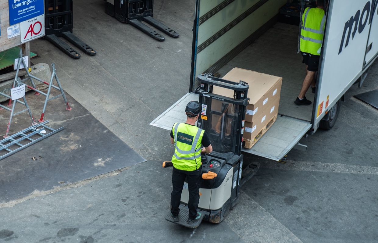 Pladsmedarbejder fra SiteHub kører en palle med pakker ud af en lastbil med en el-palleløfter